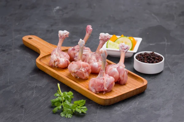 Raw chicken lollipop,six  pieces of chicken lollipop arranged on a serving board with black pepper,coriander leaf and cucumber slices on background with grey textured base