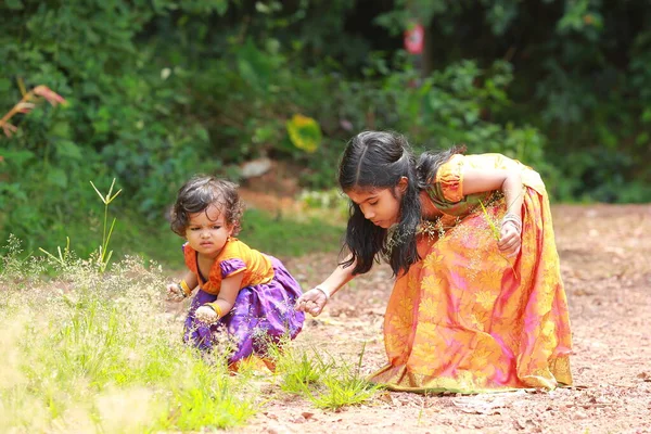 南インドの女の子の子供たちは 波状の草 緑の背景の花を摘んで 美しい伝統的なドレスの長いスカートとブラウスを着て — ストック写真