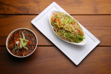 Tavuk Hakka Eriştesi ve biberli tavuk masalası, ahşap desenli beyaz servis tabağında, oval şeklinde bir tabakta servis ediliyor.