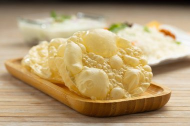 Kerala Papadum ya da sade papalık veya Appalam, ahşap desenli arka planda sebze biryani 'nin yan yemeği olarak ahşap bir tahtaya yerleştirilmiş, seçici odaklı..