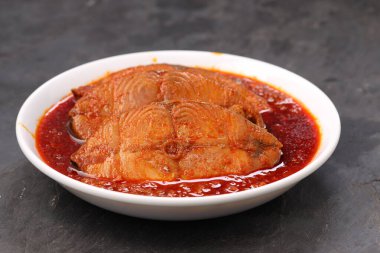 Kahin Balık köri, geleneksel Hint balığı körisi, köri yapraklarıyla süslenmiş beyaz bir seramik kasede düzenlenmiş, arpacık soğuğu ve gri dokulu arka planda taze soğuk, izole edilmiş..