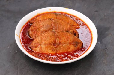 Kahin Balık köri, geleneksel Hint balığı körisi, köri yapraklarıyla süslenmiş beyaz bir seramik kasede düzenlenmiş, arpacık soğuğu ve gri dokulu arka planda taze soğuk, izole edilmiş..