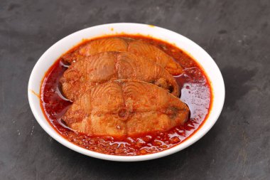 Kahin Balık köri, geleneksel Hint balığı körisi, köri yapraklarıyla süslenmiş beyaz bir seramik kasede düzenlenmiş, arpacık soğuğu ve gri dokulu arka planda taze soğuk, izole edilmiş..