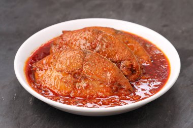 Kahin Balık köri, geleneksel Hint balığı körisi, köri yapraklarıyla süslenmiş beyaz bir seramik kasede düzenlenmiş, arpacık soğuğu ve gri dokulu arka planda taze soğuk, izole edilmiş..