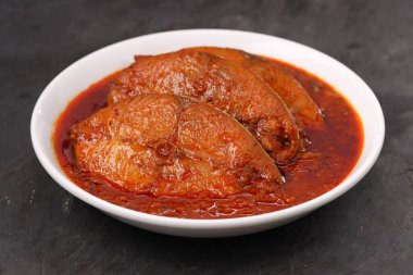 Kahin Balık köri, geleneksel Hint balığı körisi, köri yapraklarıyla süslenmiş beyaz bir seramik kasede düzenlenmiş, arpacık soğuğu ve gri dokulu arka planda taze soğuk, izole edilmiş..