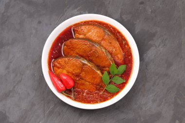 Kahin Balık köri, geleneksel Hint balığı körisi, köri yapraklarıyla süslenmiş beyaz bir seramik kasede düzenlenmiş, arpacık soğuğu ve gri dokulu arka planda taze soğuk, izole edilmiş..