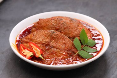 Kahin Balık köri, geleneksel Hint balığı körisi, köri yapraklarıyla süslenmiş beyaz bir seramik kasede düzenlenmiş, arpacık soğuğu ve gri dokulu arka planda taze soğuk, izole edilmiş..