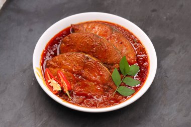 Kahin Balık köri, geleneksel Hint balığı körisi, köri yapraklarıyla süslenmiş beyaz bir seramik kasede düzenlenmiş, arpacık soğuğu ve gri dokulu arka planda taze soğuk, izole edilmiş..