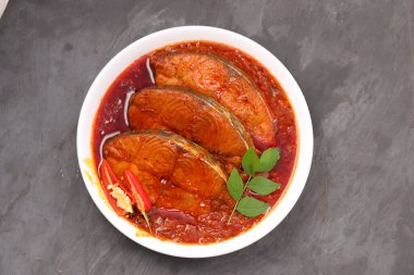 Kahin Balık köri, geleneksel Hint balığı körisi, köri yapraklarıyla süslenmiş beyaz bir seramik kasede düzenlenmiş, arpacık soğuğu ve gri dokulu arka planda taze soğuk, izole edilmiş..