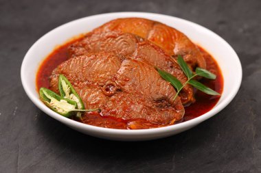 Kahin Balık köri, geleneksel Hint balığı körisi, köri yapraklarıyla süslenmiş beyaz bir seramik kasede düzenlenmiş, arpacık soğuğu ve gri dokulu arka planda taze soğuk, izole edilmiş..