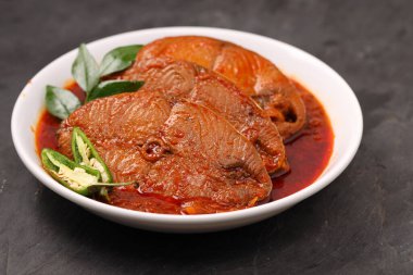 Kahin Balık köri, geleneksel Hint balığı körisi, köri yapraklarıyla süslenmiş beyaz bir seramik kasede düzenlenmiş, arpacık soğuğu ve gri dokulu arka planda taze soğuk, izole edilmiş..