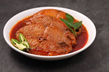 Kahin Balık köri, geleneksel Hint balığı körisi, köri yapraklarıyla süslenmiş beyaz bir seramik kasede düzenlenmiş, arpacık soğuğu ve gri dokulu arka planda taze soğuk, izole edilmiş..