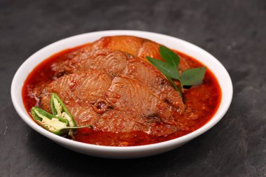 Kahin Balık köri, geleneksel Hint balığı körisi, köri yapraklarıyla süslenmiş beyaz bir seramik kasede düzenlenmiş, arpacık soğuğu ve gri dokulu arka planda taze soğuk, izole edilmiş..