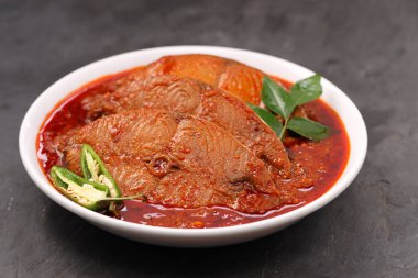 Kahin Balık köri, geleneksel Hint balığı körisi, köri yapraklarıyla süslenmiş beyaz bir seramik kasede düzenlenmiş, arpacık soğuğu ve gri dokulu arka planda taze soğuk, izole edilmiş..