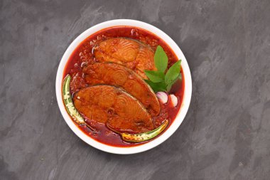 Kahin Balık köri, geleneksel Hint balığı körisi, köri yapraklarıyla süslenmiş beyaz bir seramik kasede düzenlenmiş, arpacık soğuğu ve gri dokulu arka planda taze soğuk, izole edilmiş..