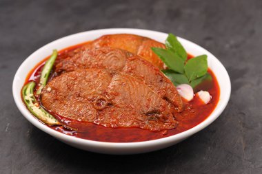 Kahin Balık köri, geleneksel Hint balığı körisi, köri yapraklarıyla süslenmiş beyaz bir seramik kasede düzenlenmiş, arpacık soğuğu ve gri dokulu arka planda taze soğuk, izole edilmiş..