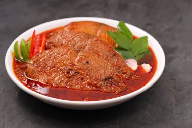 Kahin Balık köri, geleneksel Hint balığı körisi, köri yapraklarıyla süslenmiş beyaz bir seramik kasede düzenlenmiş, arpacık soğuğu ve gri dokulu arka planda taze soğuk, izole edilmiş..