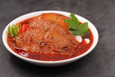 Kahin Balık köri, geleneksel Hint balığı körisi, köri yapraklarıyla süslenmiş beyaz bir seramik kasede düzenlenmiş, arpacık soğuğu ve gri dokulu arka planda taze soğuk, izole edilmiş..