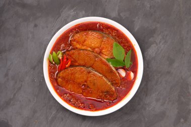 Kahin Balık köri, geleneksel Hint balığı körisi, köri yapraklarıyla süslenmiş beyaz bir seramik kasede düzenlenmiş, arpacık soğuğu ve gri dokulu arka planda taze soğuk, izole edilmiş..