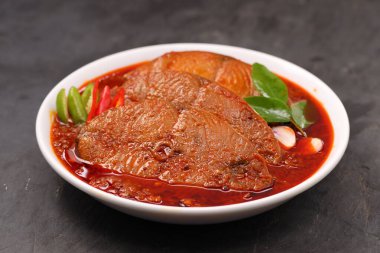 Kahin Balık köri, geleneksel Hint balığı körisi, köri yapraklarıyla süslenmiş beyaz bir seramik kasede düzenlenmiş, arpacık soğuğu ve gri dokulu arka planda taze soğuk, izole edilmiş..