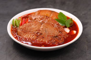 Kahin Balık köri, geleneksel Hint balığı körisi, köri yapraklarıyla süslenmiş beyaz bir seramik kasede düzenlenmiş, arpacık soğuğu ve gri dokulu arka planda taze soğuk, izole edilmiş..