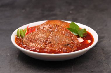 Kahin Balık köri, geleneksel Hint balığı körisi, köri yapraklarıyla süslenmiş beyaz bir seramik kasede düzenlenmiş, arpacık soğuğu ve gri dokulu arka planda taze soğuk, izole edilmiş..