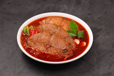 Kahin Balık köri, geleneksel Hint balığı körisi, köri yapraklarıyla süslenmiş beyaz bir seramik kasede düzenlenmiş, arpacık soğuğu ve gri dokulu arka planda taze soğuk, izole edilmiş..