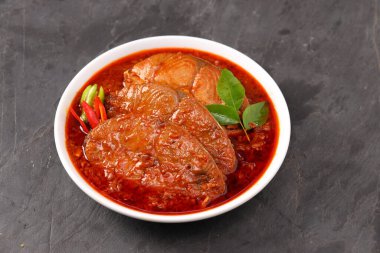 Kahin Balık köri, geleneksel Hint balığı körisi, köri yapraklarıyla süslenmiş beyaz bir seramik kasede düzenlenmiş, arpacık soğuğu ve gri dokulu arka planda taze soğuk, izole edilmiş..