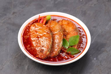 Kahin Balık köri, geleneksel Hint balığı körisi, köri yapraklarıyla süslenmiş beyaz bir seramik kasede düzenlenmiş, arpacık soğuğu ve gri dokulu arka planda taze soğuk, izole edilmiş..