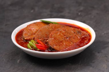 Kahin Balık köri, geleneksel Hint balığı körisi, köri yapraklarıyla süslenmiş beyaz bir seramik kasede düzenlenmiş, arpacık soğuğu ve gri dokulu arka planda taze soğuk, izole edilmiş..