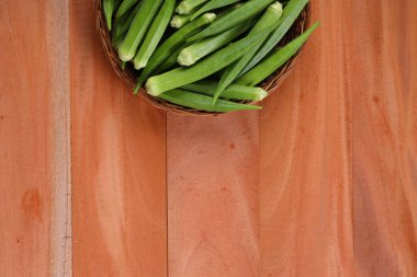  Bamya ya ya da Lady 'nin parmağı ya da ahşap desenli arka plan, izole ve seçici odaklı bir sepete yerleştirilmiş taze Bhindi sebzesi.