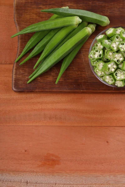 Okra or Lady\'s finger or Bhindi fresh green vegetable arranged  on a wooden board with a glass bowl full of okra sliced rings  with wooden background, selective focus ,top view.