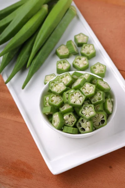 Okra or Lady\'s finger or Bhindi fresh green vegetable arranged  on a white tableware with a  bowl full of okra sliced rings with wooden background, selective focus