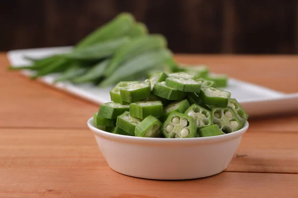 Okra or Lady\'s finger or Bhindi fresh green vegetable arranged  on a white tableware with a  bowl full of okra sliced rings with wooden background, selective focus