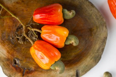 Kaju fıstığı elması ve kaju tohumları beyaz arkaplana yerleştirilmiş ahşap bir parça üzerinde sıralanmış, seçici odak.