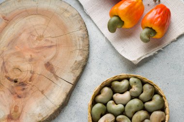 Kaju fıstığı elması ve kaju tohumları gri desenli bir arka planda sıralanmış ve ahşap bir parça yakın, üst görünüm.