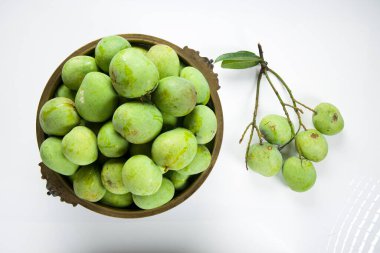 Çiğ mango geleneksel olarak pirinç bir kap ve yakın bir yere yerleştirilmiş yeşil mango beyaz desenli arka plan.