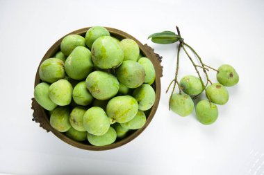 Çiğ mango geleneksel olarak pirinç bir kap ve yakın bir yere yerleştirilmiş yeşil mango beyaz desenli arka plan.