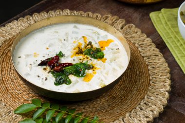 Pachadi ya da Raitha Güney Hindistan mezesi kül koruyucusu, kaymak ve hindistan cevizi kullanarak ahşap arka planda, izole edilmiş pirinç bir kaba yerleştirilir..