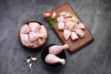 Çiğ tavuk pirzolası, derisiz tavuk pirzolası, tavuk kızartması ve ahşap bir tahtada kişniş yaprağı, domates dilimleri, sarımsak karanfili ve gri dokuda biber kombinasyonu, seçici odaklı.