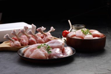 Çiğ tavuk kesim kombinasyonu, tavuk biryani kesimi, tavuk kızartması ve tavuk lolipopu kombinasyonu kişniş yaprağı, sarımsak karanfili, yağ ve biber içeren ahşap bir tahtada düzenlenmiş gri desenli arka planda ambalaj kutusu