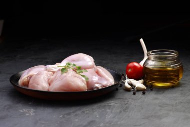 Çiğ tavuk biryani derisiz kesilmiş siyah kabın üzerinde düzenlenmiş ve kişniş yaprağı, yağ, domates, karanfil sarımsak ve biber ile süslenmiş taş desenli arka planda
