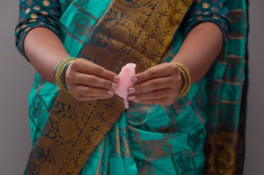 Yeniden kullanılabilir silikon regl kupası tutan Hintli bir kadın ve farklı katlama çeşitleri gösteriyor.