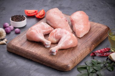 Taze derisiz çiğ tavuk bacakları, bagetler ve çiğ tavuk göğsü kahverengi ahşap bir tabanda gri desenli arka planda..