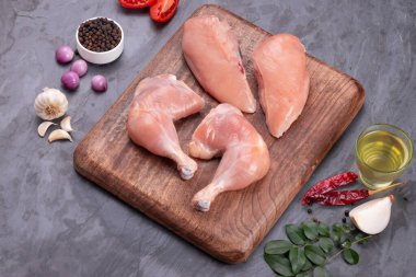 Taze derisiz çiğ tavuk bacakları, bagetler ve çiğ tavuk göğsü kahverengi ahşap bir tabanda gri desenli arka planda..