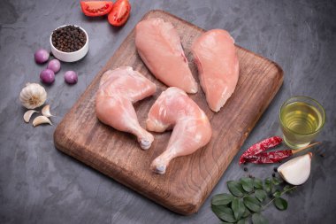 Taze derisiz çiğ tavuk bacakları, bagetler ve çiğ tavuk göğsü kahverengi ahşap bir tabanda gri desenli arka planda..