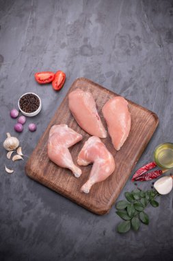 Taze derisiz çiğ tavuk bacakları, bagetler ve çiğ tavuk göğsü kahverengi ahşap bir tabanda gri desenli arka planda..