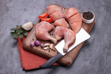 Taze derisiz çiğ tavuk bacakları, bagetler ve çiğ tavuk göğsü kahverengi ahşap bir tabanda gri desenli arka planda..