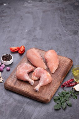 Taze derisiz çiğ tavuk bacakları, bagetler ve çiğ tavuk göğsü kahverengi ahşap bir tabanda gri desenli arka planda..