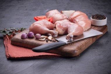 Taze derisiz çiğ tavuk bacakları, bagetler ve çiğ tavuk göğsü kahverengi ahşap bir tabanda gri desenli arka planda..